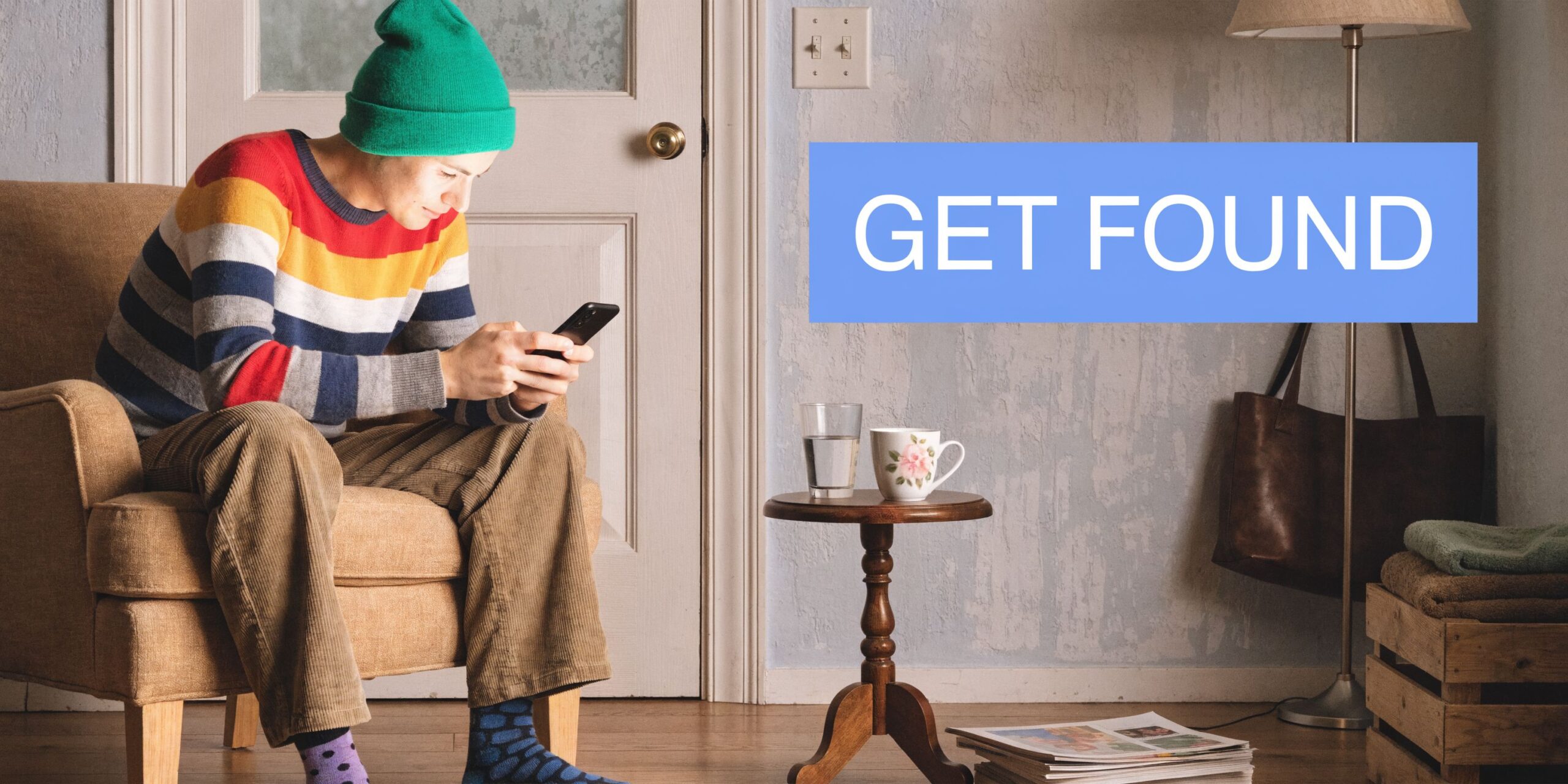 A person wearing a green beanie and colorful sweater sitting in a chair checking their phone.