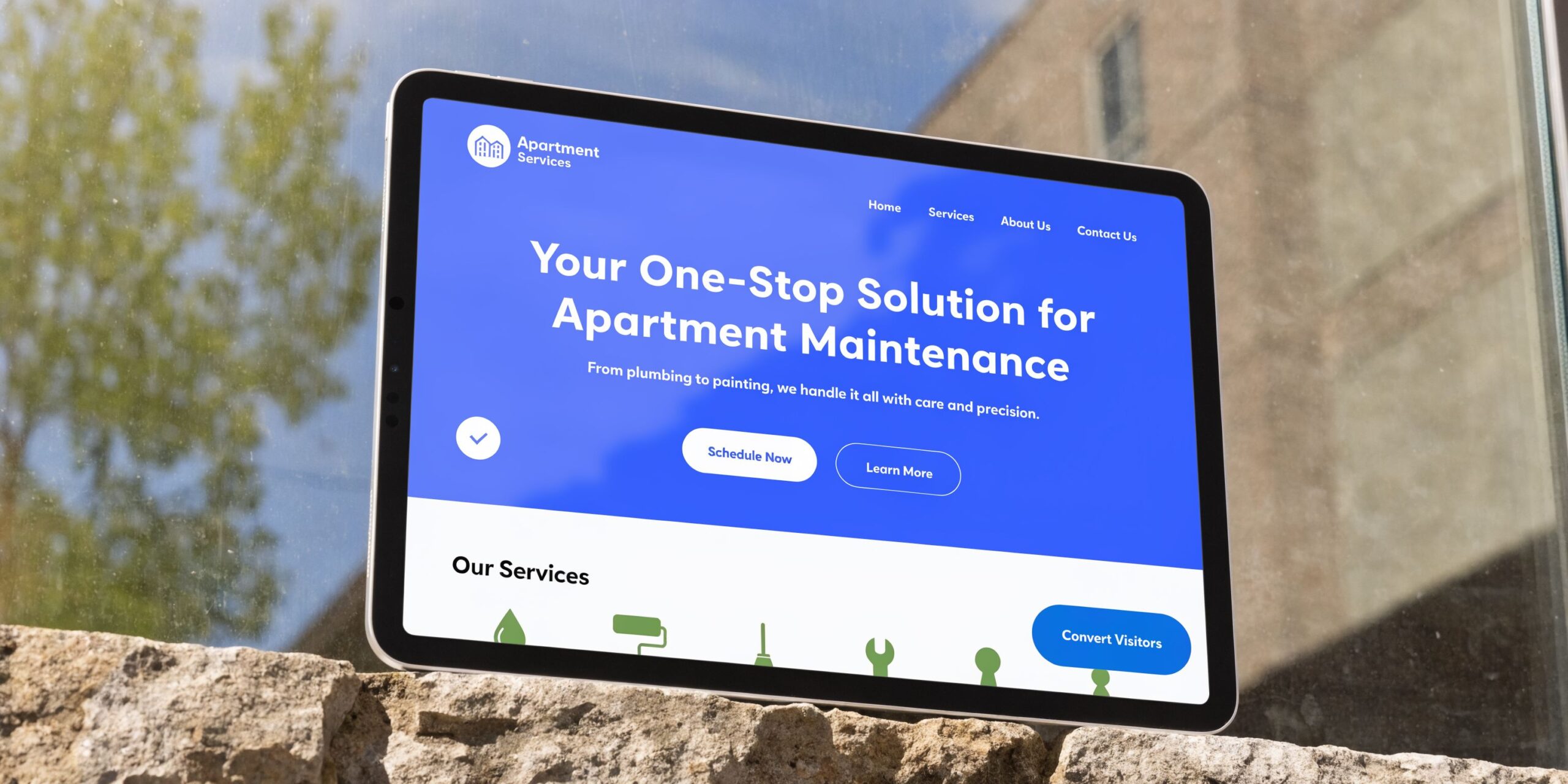 A digital tablet displaying an apartment maintenance company website design leaning against a stone wall outdoors.