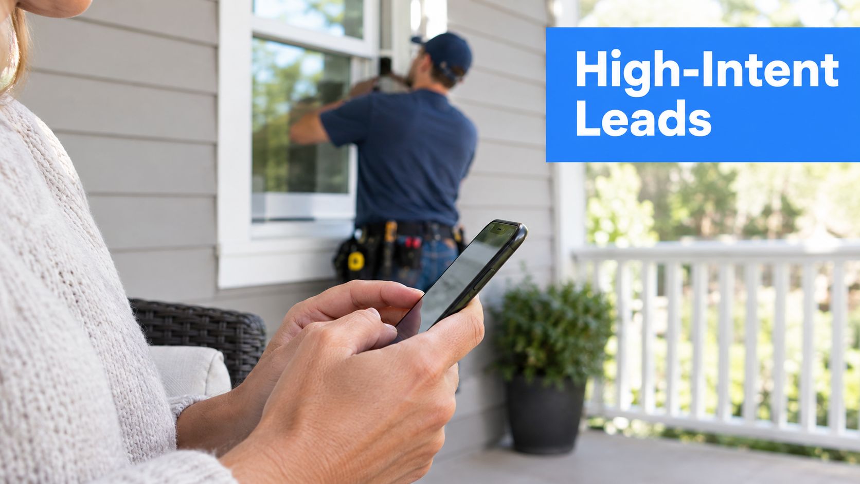 A customer using a smartphone while a professional contractor installs windows in the background on a porch.